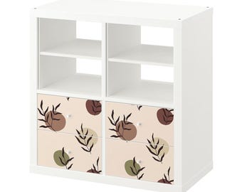 May include: White cube shelf unit with four drawers. The drawers have a beige background with brown and green abstract leaf and circle patterns.