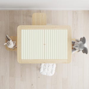 Puede incluir: Vista aérea de un juego de mesa y silla para niños de madera clara. La mesa tiene un diseño a rayas en la parte superior. Una silla pequeña, un conejito de peluche, un elefante de peluche y un cojín blanco rodean la mesa.