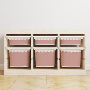 Può includere: Un mobile contenitore in legno con sei scomparti, ciascuno con un contenitore rosa e bianco. I contenitori hanno un bordo smerlato. L'unità è in legno chiaro e poggia su un pavimento in legno.