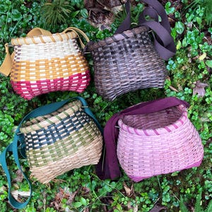 May include: Four woven baskets with adjustable fabric straps. One basket features horizontal stripes of white, yellow, and red. One is dark brown. One has green and tan woven patterns. One is solid pink with a matching dark pink fabric strap.
