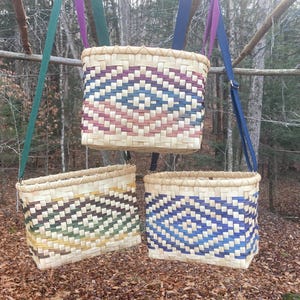 May include: Three woven baskets with colourful geometric patterns hanging from straps. The baskets are made of natural materials and have a rustic, handmade look.