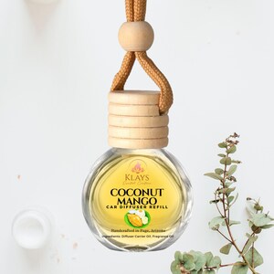 May include: A clear, round car air freshener refill with a wooden top and a woven cord for hanging. The label reads "COCONUT MANGO" and "CAR DIFFUSER REFILL". The liquid inside is yellow. The product is handcrafted in Page, Arizona.