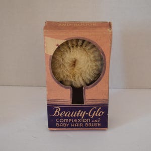 May include: Vintage "Beauty-Glo" complexion and baby hair brush in its original box. The box is peach-colored with a dark purple label. The brush is visible through a circular opening.