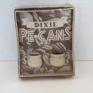 May include: A boxed set of Dixie Pecans, featuring a brown and white design. The packaging includes the text "Dixie Pecans" in large, bold letters, and two small, off-white ceramic cups.