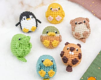 May include: A collection of crocheted animal amigurumi toys. The toys include a penguin, a duck, a beaver, a frog, a duckling, and a chick. The toys are all made with different coloured yarn and have different facial expressions.