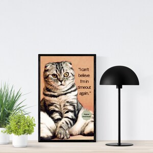 May include: A black and white cat with folded ears sits in a framed digital download print. The cat is looking at the camera with a serious expression. The text in the print reads "I can't believe I'm in timeout again."