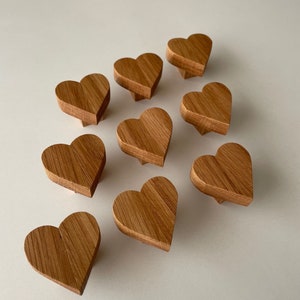 Może przedstawiać: Dziesięć drewnianych gałek do szuflad w kształcie serca w jasnobrązowym kolorze. Gałki są ułożone w półkole na białym tle.