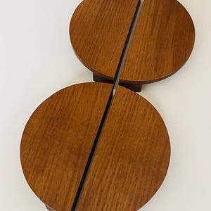 Może przedstawiać: Dwa zestawy drewnianych podkładek, każdy składający się z dwóch półkolistych elementów. Podkładki mają ciepły brązowy kolor z widocznym usłojeniem drewna. Zostały zaprojektowane tak, aby pasowały do siebie i tworzyły pełne koło. Podkładki leżą na białej powierzchni.