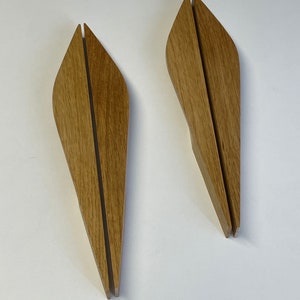 Peut inclure: Deux poignées de tiroir en bois en forme de larme avec une fente au centre. Les poignées sont de couleur brun clair.