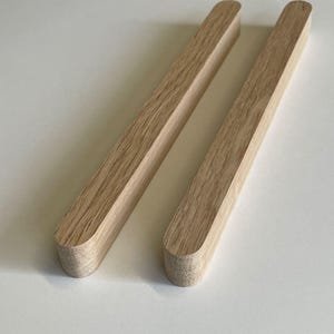 Op de afbeelding: Twee houten deuvels met afgeronde uiteinden. De deuvels zijn lichtbruin van kleur en hebben een gladde, gepolijste afwerking.