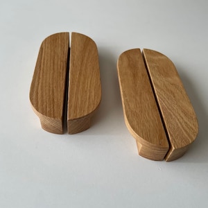 Op de afbeelding: Twee houten kastgrepen met een afgeronde ovale vorm en een gesplitst ontwerp. De grepen zijn gemaakt van lichtbruin hout met een natuurlijke houtnerf.