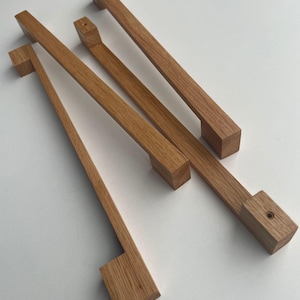 May include: Four wooden cabinet pulls with a square shape and a natural wood finish.