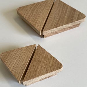 Op de afbeelding: Twee driehoekige houten kastdeurgrepen met een natuurlijke houtkleur.