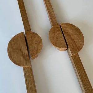 Peut inclure: Deux couverts à salade en bois. Chaque couvert a un long manche rectangulaire et une tête semi-circulaire. Le bois est de couleur brun clair naturel avec un grain visible. La tête de chaque couvert est divisée en deux parties.