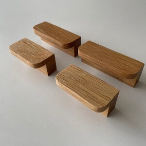 May include: Four wooden cabinet knobs with a rounded edge. The knobs are made of light brown wood with a natural grain pattern.