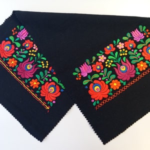 May include: Two black fabric placemats with colorful embroidered floral designs. The designs feature red, pink, yellow, green, and blue flowers.