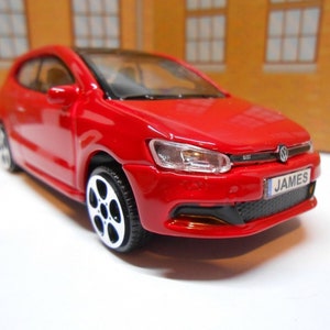 May include: Red toy car model of a Volkswagen Polo GTI with black wheels and a number plate that reads "JAMES".