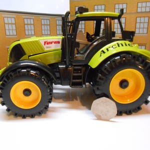 May include: A lime green and black toy tractor with large black tyres and yellow wheel centres. The tractor has the word "Farm" and the name "Archie" printed on it. The tractor is a toy.