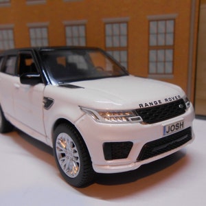 May include: White toy car model of a Range Rover with a black roof and black grille. The car has a number plate that says "JOSH".