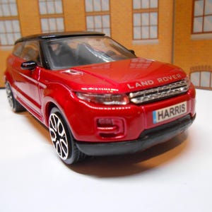 May include: Red toy car model of a Land Rover Range Rover Evoque with a black roof and black wheels. The car has a number plate that reads "HARRIS".