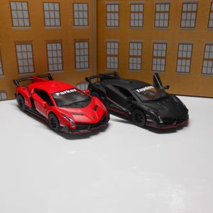 May include: Two toy sports cars, one red and one black, are displayed on a white surface. The red car has the name "Parker" on the hood, while the black car has "Zayden". Both cars have detailed designs, including spoilers and black wheels.