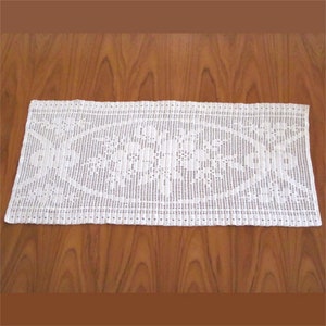 May include: White crocheted table runner with a delicate floral pattern. The runner is made of fine yarn and has a delicate lace trim.