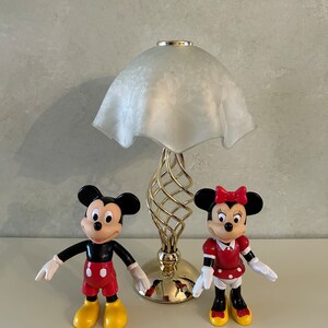 May include: A gold table lamp with a white frosted glass shade.  Mickey Mouse and Minnie Mouse figurines are in front of the lamp.
