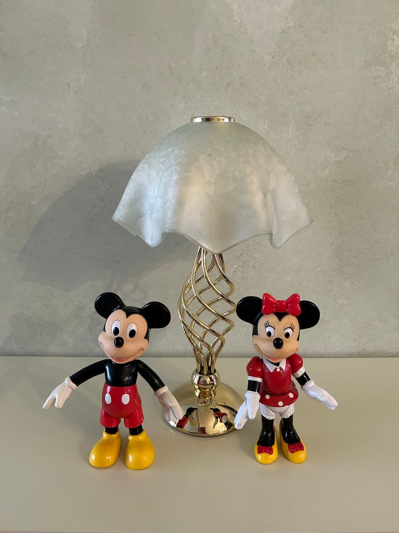 May include: A gold table lamp with a white frosted glass shade.  Mickey Mouse and Minnie Mouse figurines are in front of the lamp.