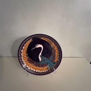 May include: A blue and white ceramic plate with a yellow, orange, red, green, and blue bird design. The bird is a crane with its wings spread out.