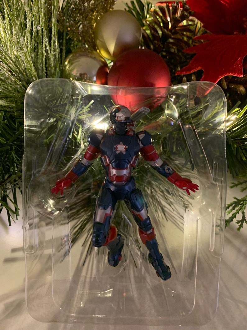 May include: A red, white and blue Iron Man Christmas ornament. The ornament is in clear plastic packaging.