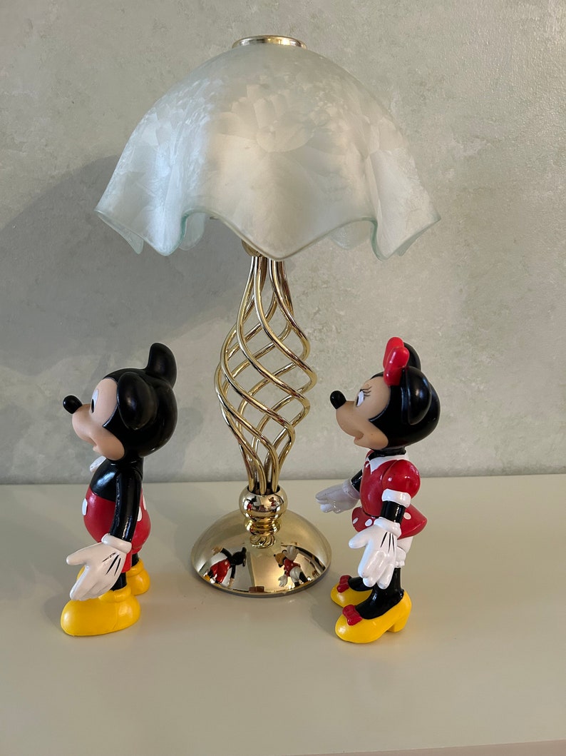 May include: A gold metal lamp with a white frosted glass shade.  Two plastic figurines of Mickey Mouse and Minnie Mouse stand in front of the lamp.