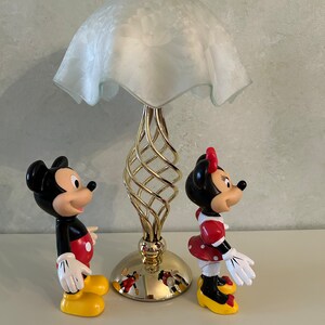 May include: A gold table lamp with a white frosted glass shade and a spiral base.  Mickey Mouse and Minnie Mouse figurines stand on either side of the lamp.