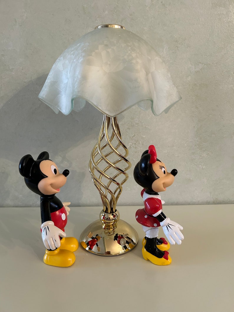 May include: A gold table lamp with a white frosted glass shade and a spiral base.  Mickey Mouse and Minnie Mouse figurines stand on either side of the lamp.