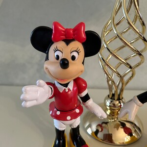 May include: A red and white polka dot dress with a red bow on top of the head. The figure has black shoes with yellow soles and a black and white face. The figure is a plastic toy of a cartoon character.