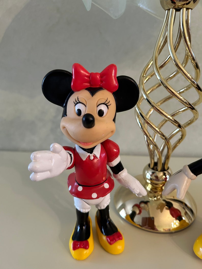 May include: A red and white polka dot dress with a red bow on top of the head. The figure has black shoes with yellow soles and a black and white face. The figure is a plastic toy of a cartoon character.