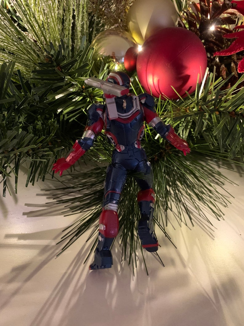 May include: A red, white and blue action figure of a superhero in a flying pose. The figure is posed as if it is hanging from a Christmas tree.