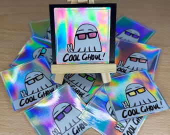 May include: A stack of iridescent holographic stickers featuring a cartoon ghost wearing 3D glasses and the text "COOL GHOUL!"