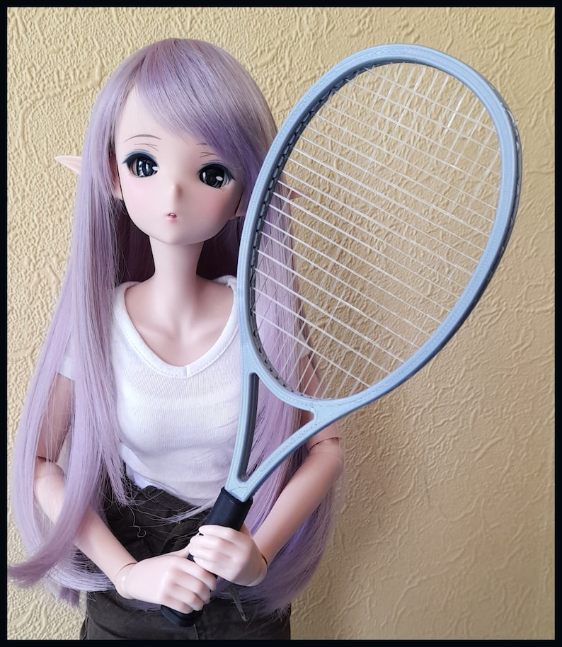 May include: A doll with long, lavender hair and a white shirt holds a light blue tennis racket with a black grip. The doll has large eyes and is posed against a textured, yellow background.