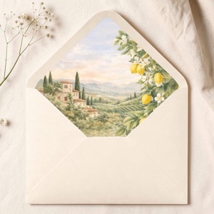 Puede incluir: Un sobre abierto, de color crema, revela un paisaje acuarelado de una villa toscana, cipreses y colinas. Un limonero con frutos amarillos y flores blancas enmarca la escena. El sobre est&aacute; sobre una superficie color crema.