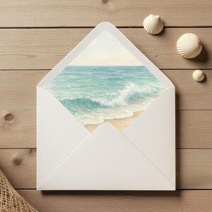 May include: A white envelope with a watercolor painting of a beach scene. The painting shows a turquoise ocean with waves crashing on a sandy shore. Three white seashells are scattered on a wooden surface.