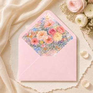 Puede incluir: Un sobre rosa claro con un dise&ntilde;o floral en el interior. El sobre abierto revela una pintura de acuarela de varias flores en tonos de rosa, naranja, amarillo y azul. El sobre est&aacute; sobre una superficie texturizada blanquecina.