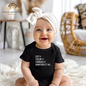 May include: A baby wearing a black bodysuit with the text "CUT ♥ COLOR ♥ CUDDLES ♥ MOM DOES IT ALL" and a white turban headband.