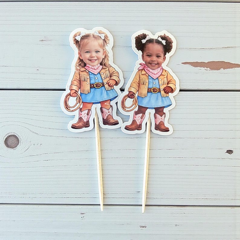 K&ouml;nnte beinhalten: Zwei Cupcake-Topper mit Illustrationen junger M&auml;dchen in Cowboy-Outfits. Jedes M&auml;dchen tr&auml;gt ein blaues Kleid, Cowboy-Stiefel, ein rosa Halstuch und eine Jacke mit Fransen. Ein M&auml;dchen ist blond, das andere hat dunkle Haare.