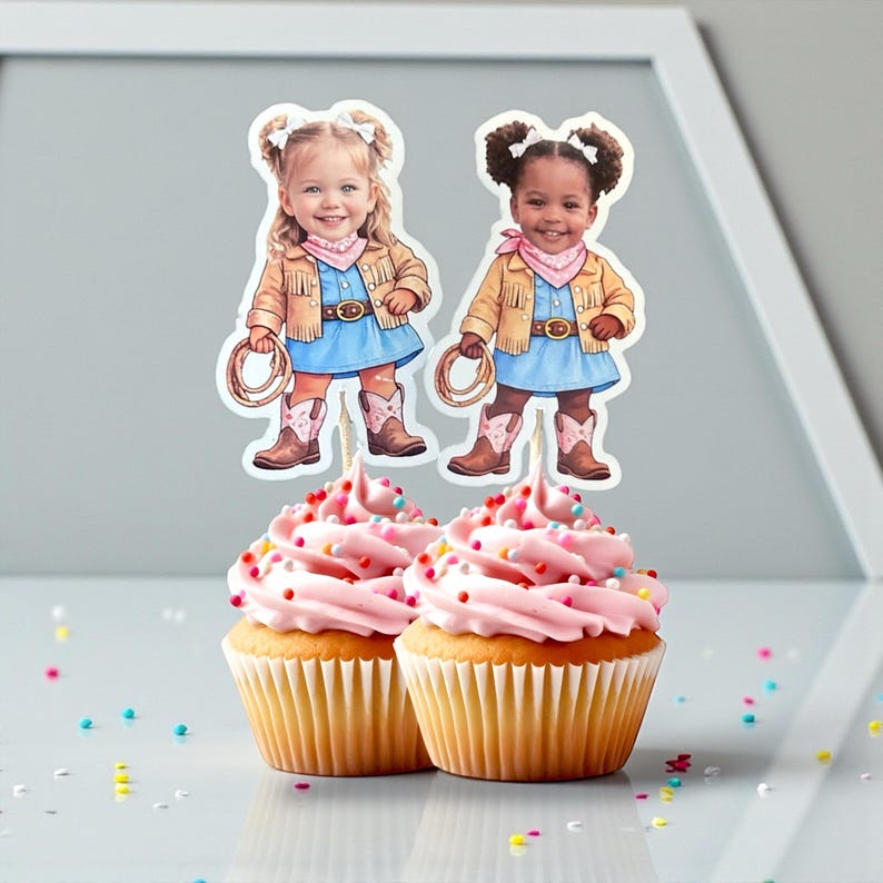 K&ouml;nnte beinhalten: Zwei Cupcakes mit rosa Zuckerguss und bunten Streuseln, gekr&ouml;nt von Cowboy-Girl-Kuchenaufs&auml;tzen. Die Aufs&auml;tze zeigen Illustrationen von M&auml;dchen in Cowboy-Kleidung, einschlie&szlig;lich H&uuml;ten, Jacken und Stiefeln. Die Cupcakes stehen auf einer reflektierenden Oberfl&auml;che.