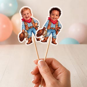 May include: Two cowboy-themed cupcake toppers. Each topper features a cartoon illustration of a child dressed in a cowboy outfit, complete with a hat, boots, and a red bandana. The toppers are held by wooden sticks.