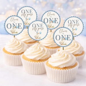 May include: Cupcakes with white frosting and decorative toppers. The toppers are round with a scalloped edge, featuring a goose illustration, the text "Oliver is ONE" and "ONE silly goose" in blue.