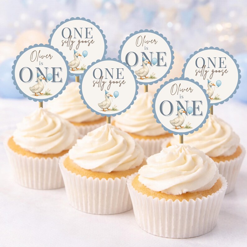 May include: Cupcakes with white frosting and decorative toppers. The toppers are round with a scalloped edge, featuring a goose illustration, the text "Oliver is ONE" and "ONE silly goose" in blue.