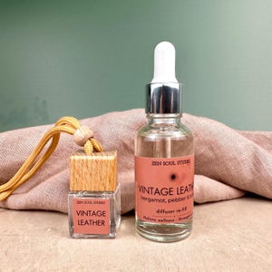 May include: Two glass bottles, one with a dropper, and a small wooden car air freshener. The labels read "VINTAGE LEATHER". The larger bottle also says "bergamot, pebber & to" and "diffuser re-fill". The air freshener has a gold cord.