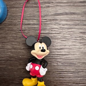 May include: A red and black plastic Mickey Mouse ornament with a red ribbon for hanging.