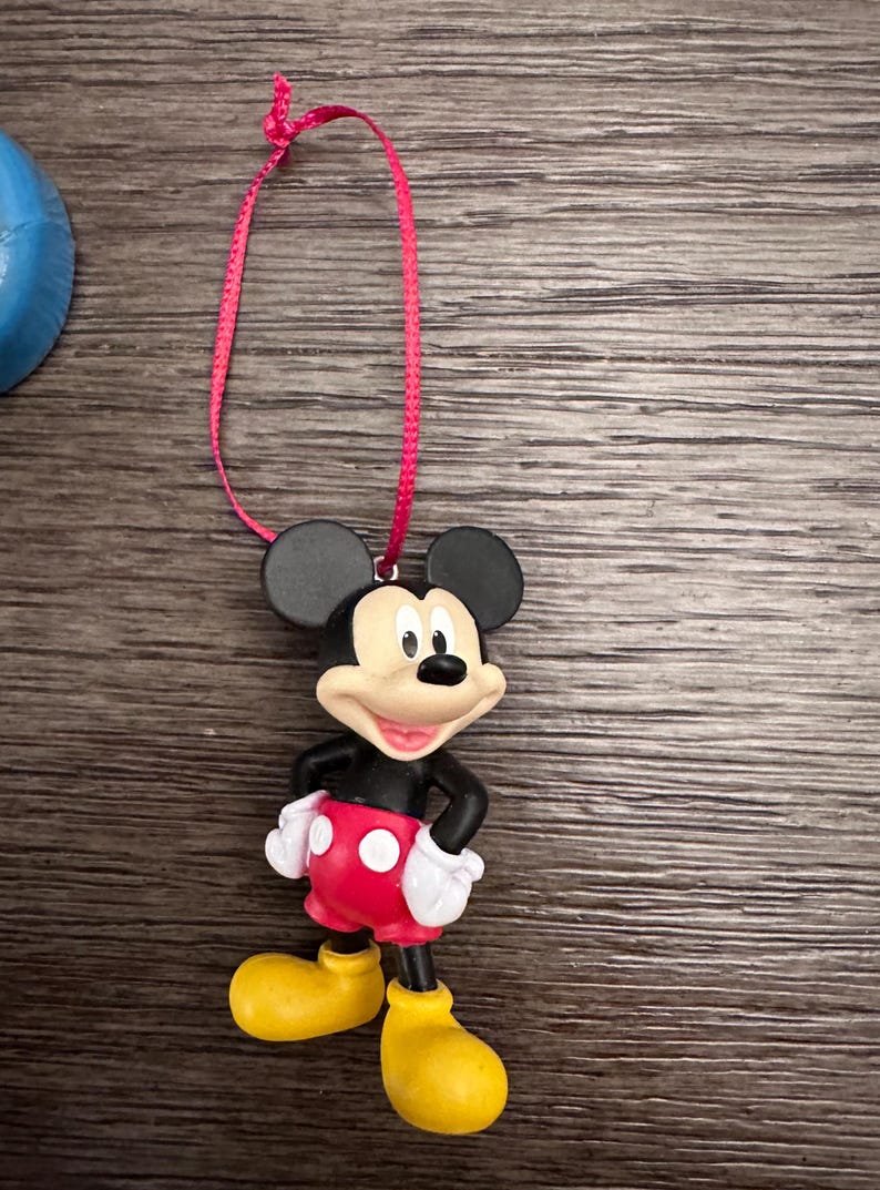 May include: A red and black plastic Mickey Mouse ornament with a red ribbon for hanging.